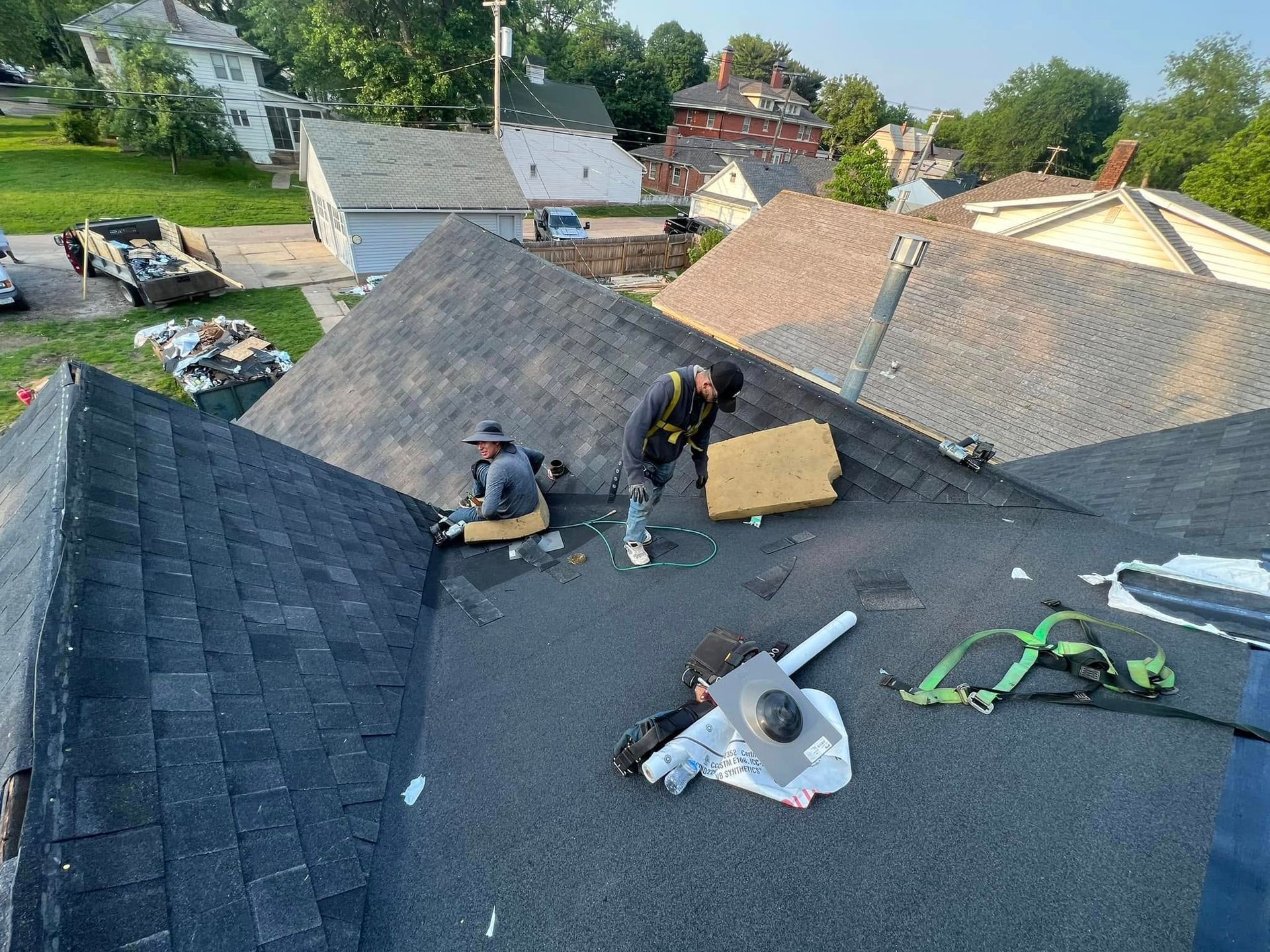 Workers repairing a gray shingled roof, with tools and materials spread across the surface.