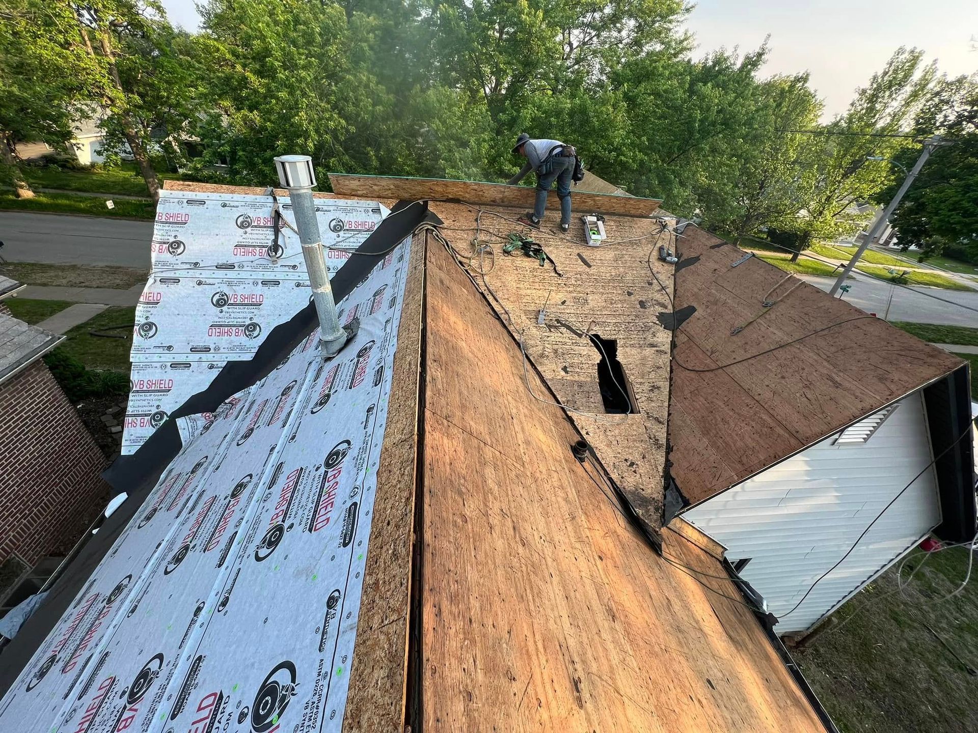 Workers reroofing a house, with exposed plywood, shingles, and underlayment visible.