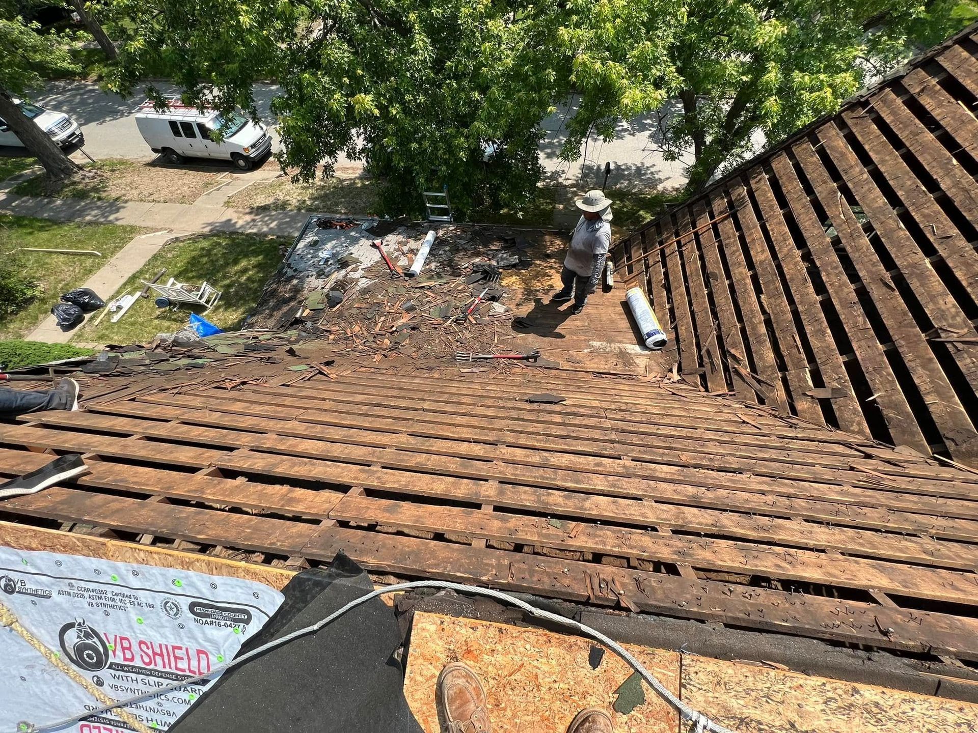 Roof view looking down at a debris-strewn yard with trees and a parked white car