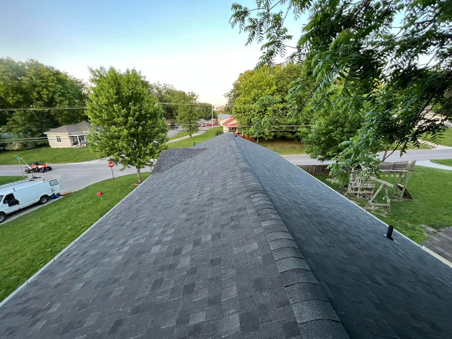 View from a rooftop over a suburban neighborhood with trees, houses, and a parked car on a sunny day