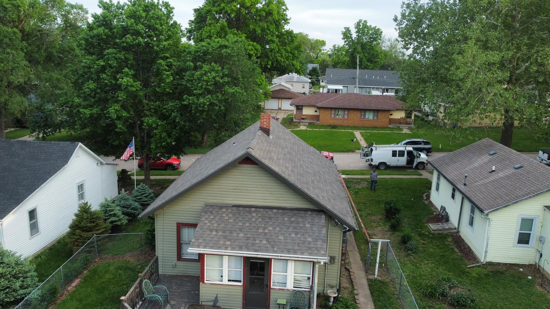 Aerial view of a small neighborhood with houses, trees, and parked cars on a rainy day