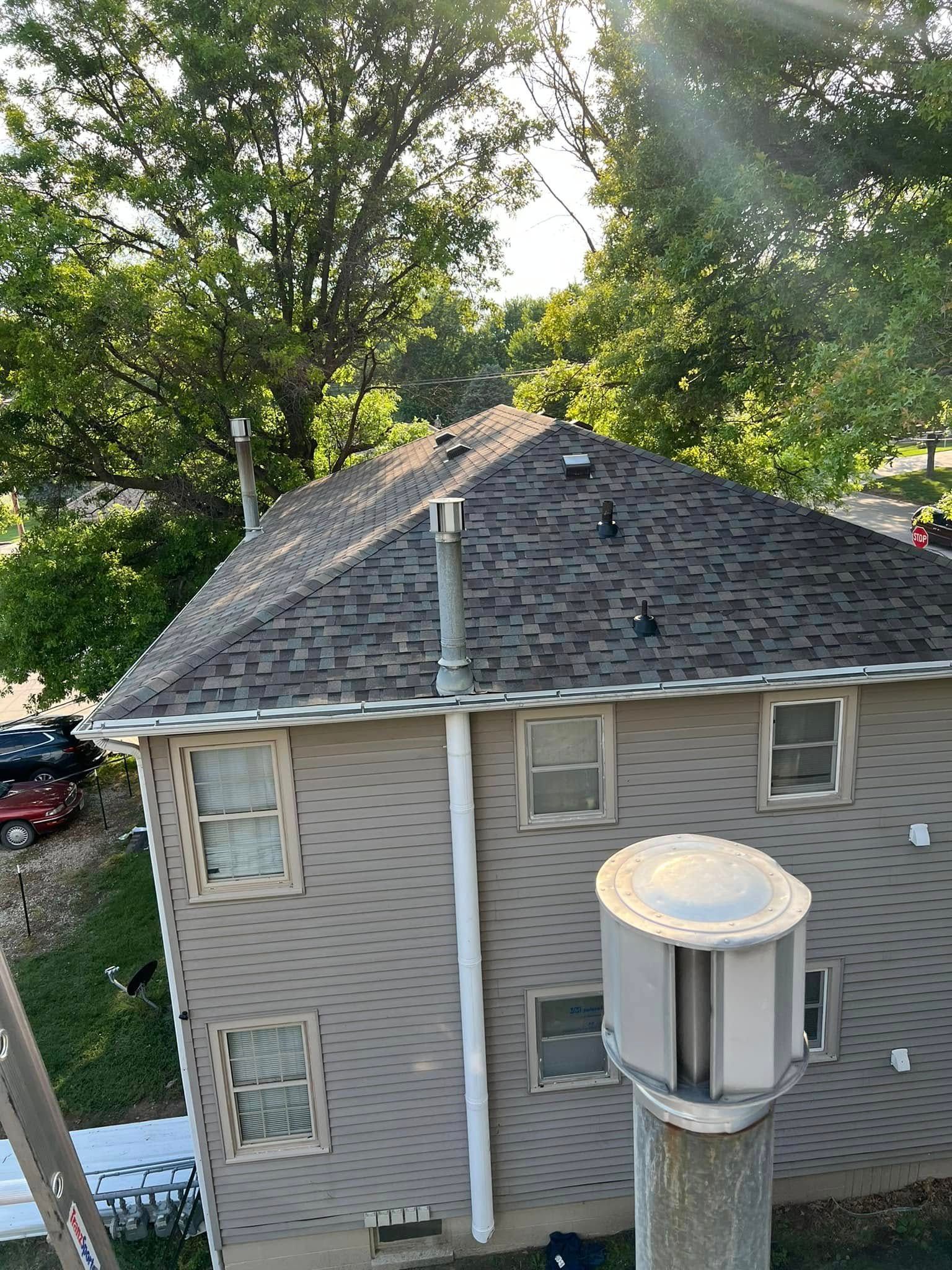 Two-story house with gray siding and dark shingled roof, seen from above through trees.