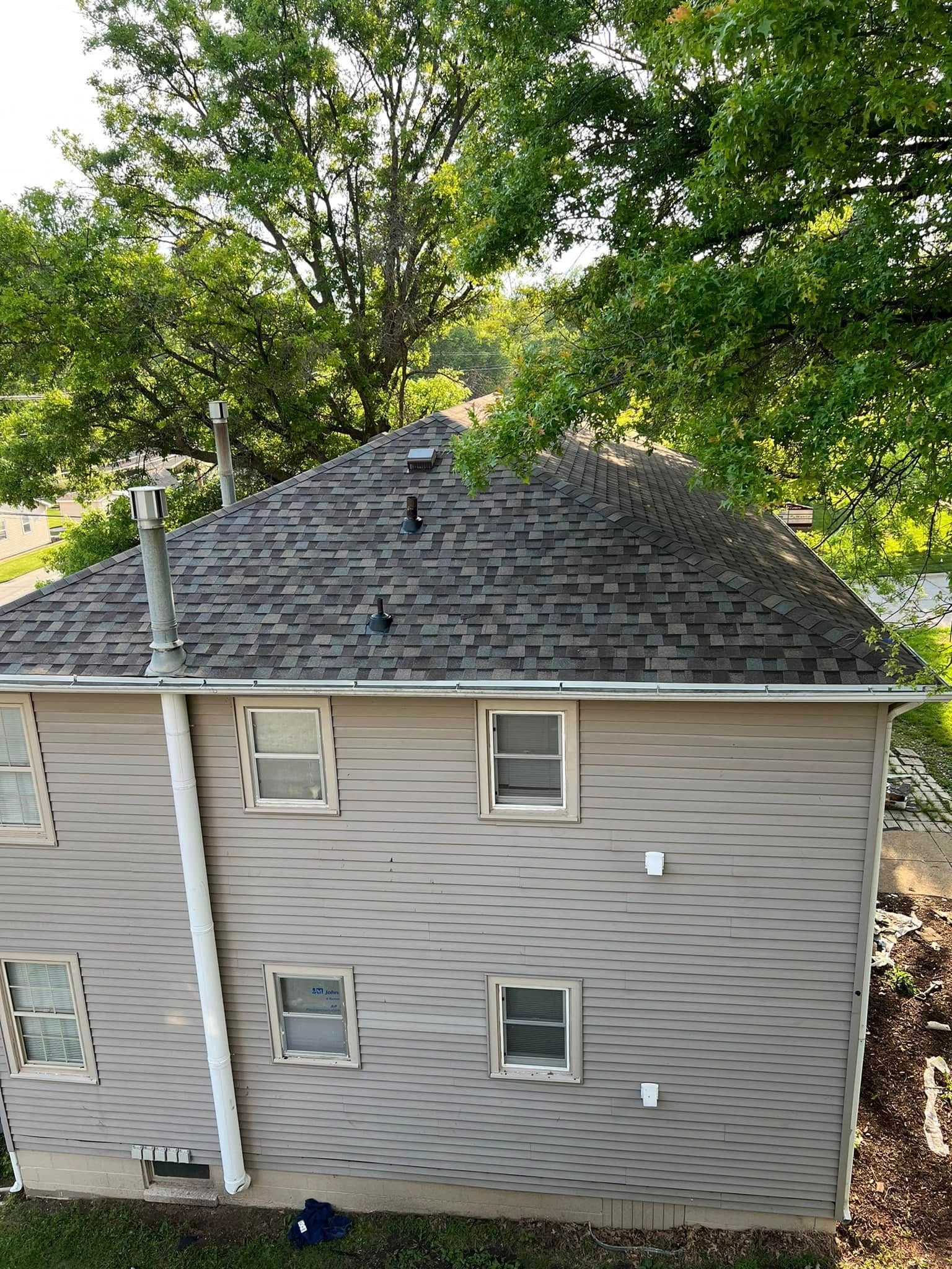 Side view of a gray two-story house with small windows and trees behind it