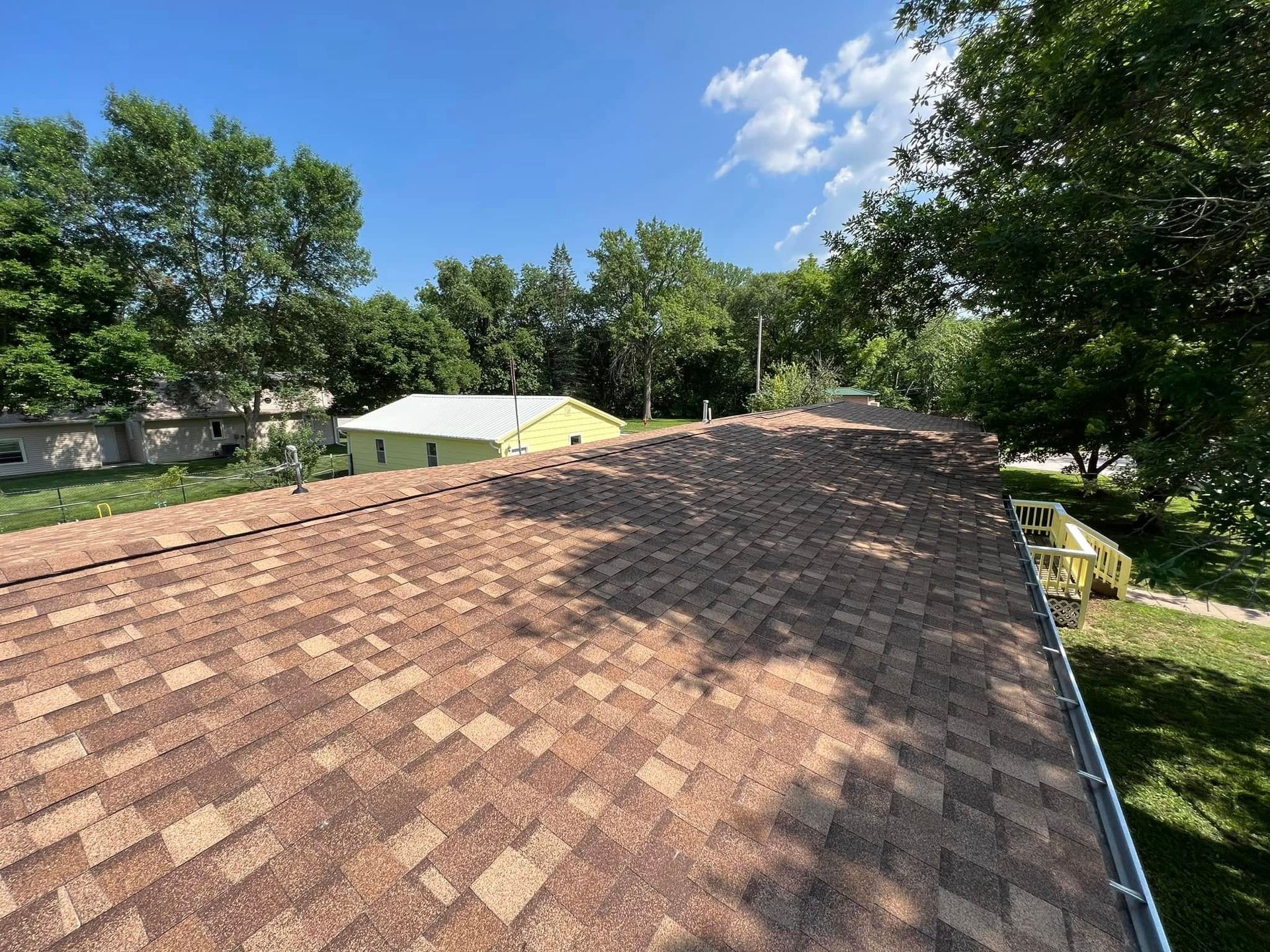 Shingled roof with trees and a blue sky in the background