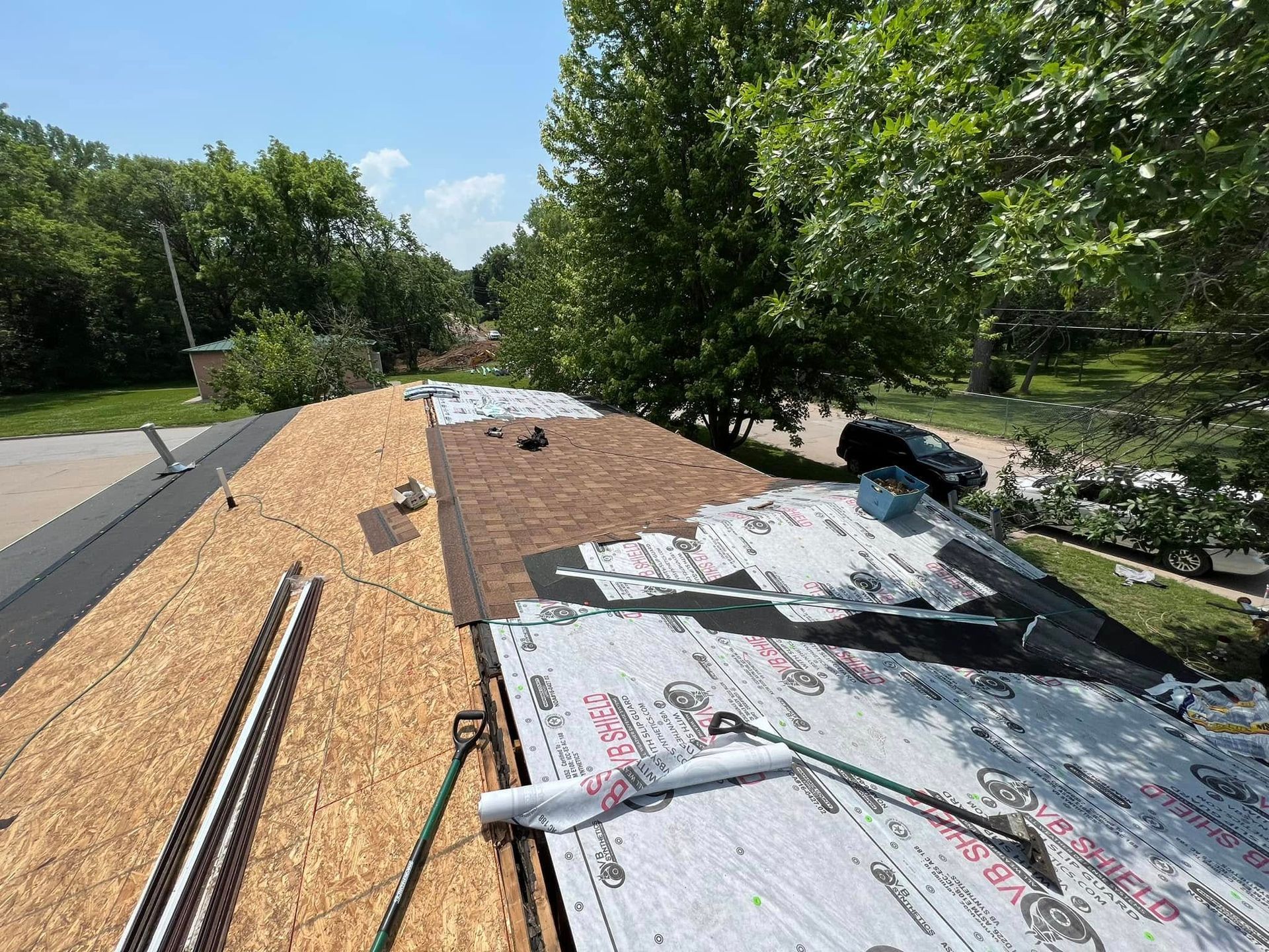 Rooftop under construction with plywood, roofing felt, and trees in the background