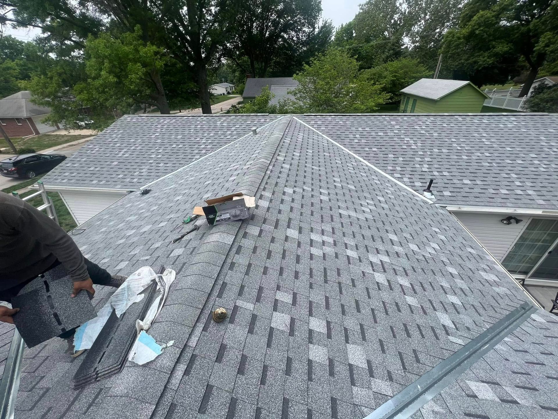 Roofing workers repairing a gray shingle roof on a house, with tools spread across the ridge