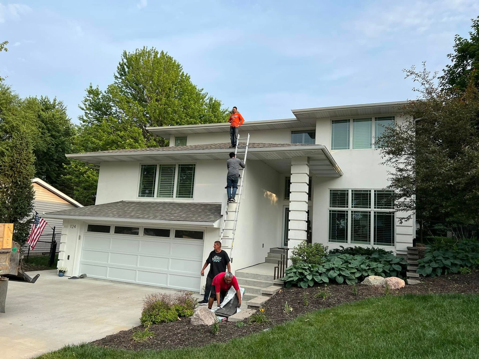 Workers on a house roof and near the front steps, inspecting or repairing the exterior.