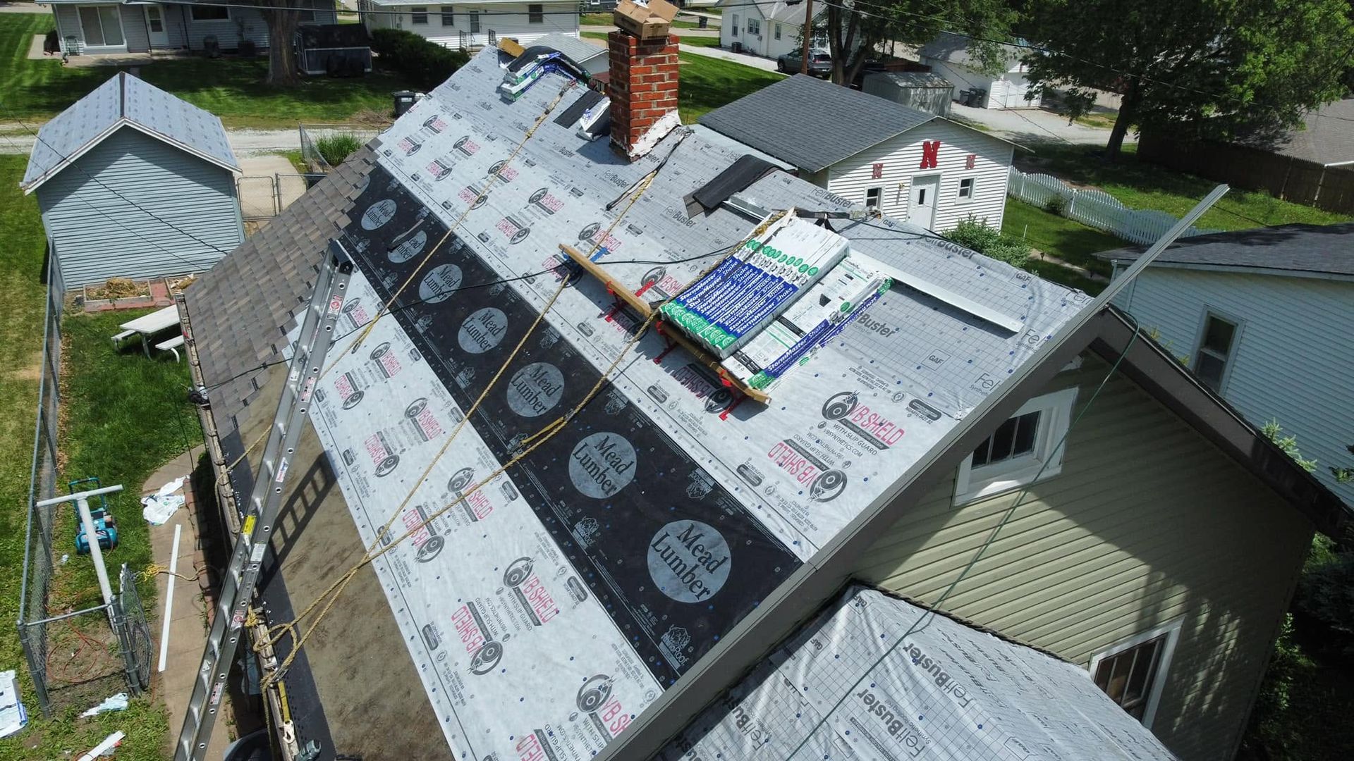 Roof under repair with black underlayment, shingles being installed, and workers’ equipment on top