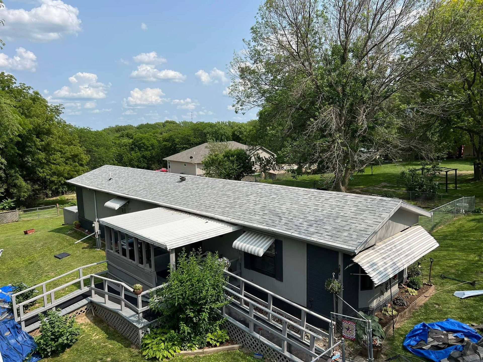 Dark-gray house with white railings and awnings in a green yard under a partly cloudy sky.