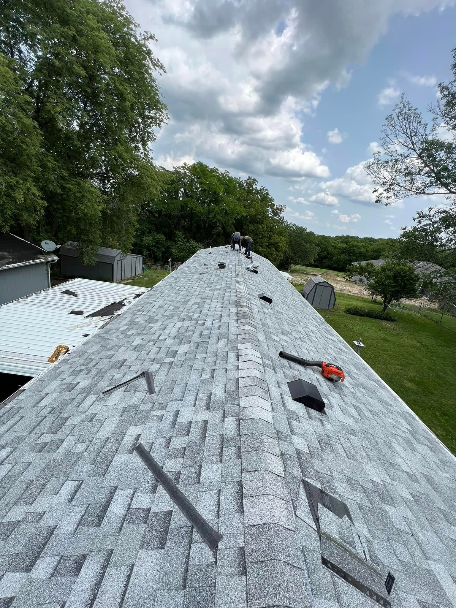 Roof covered with gray underlayment, with tools on top and trees and sky in the background