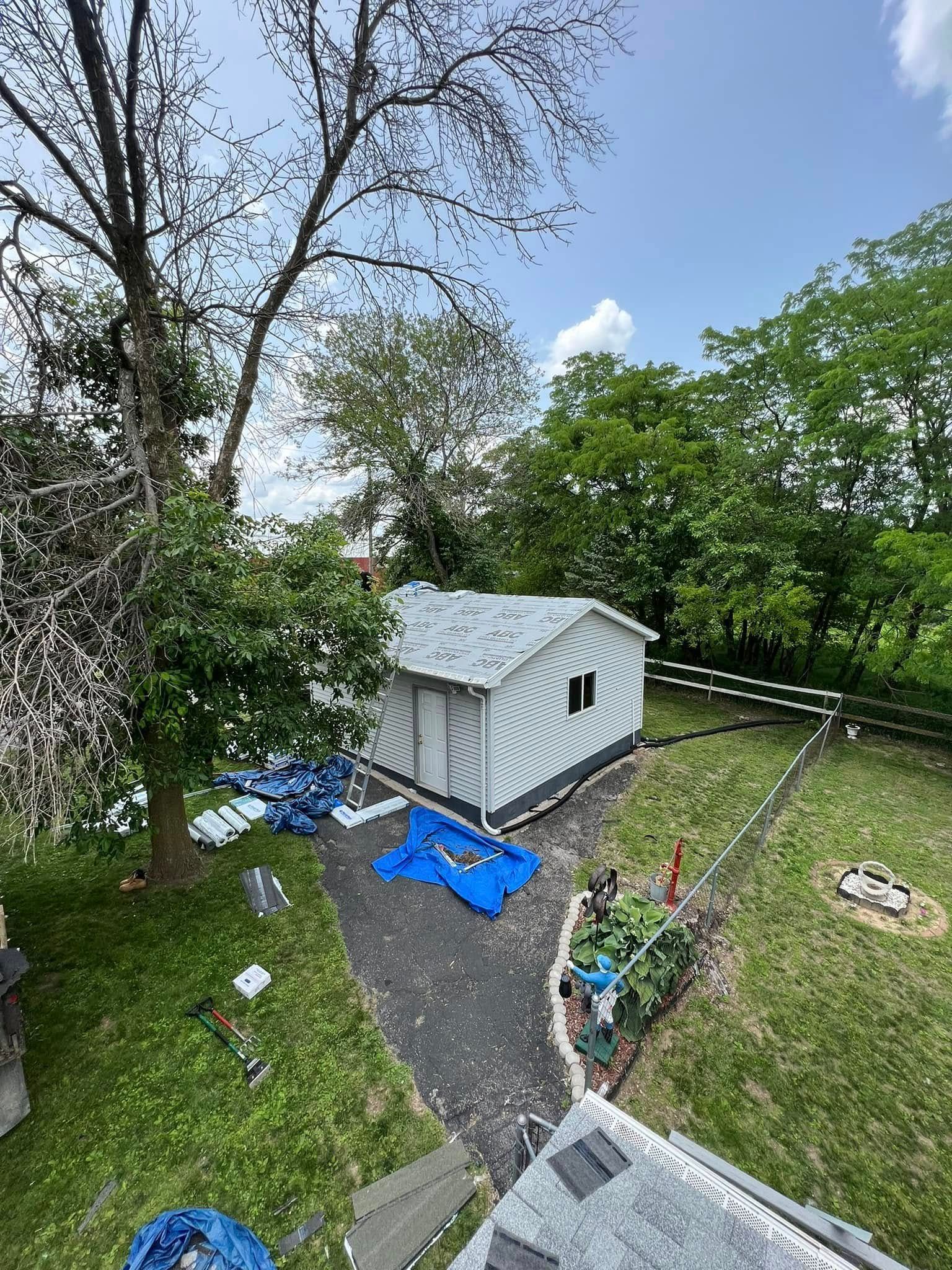 Backyard with white shed, blue tarp, gravel path, and green trees under a sunny sky