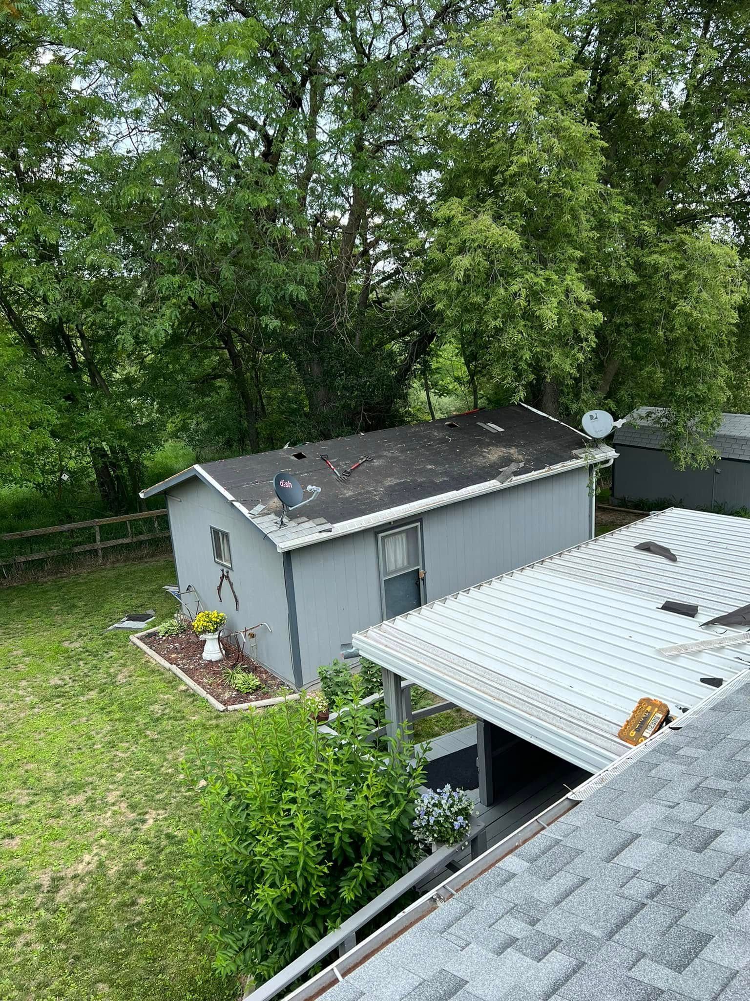 Backyard with a gray shed, leafy trees, and a rooftop/covered structure in the foreground.