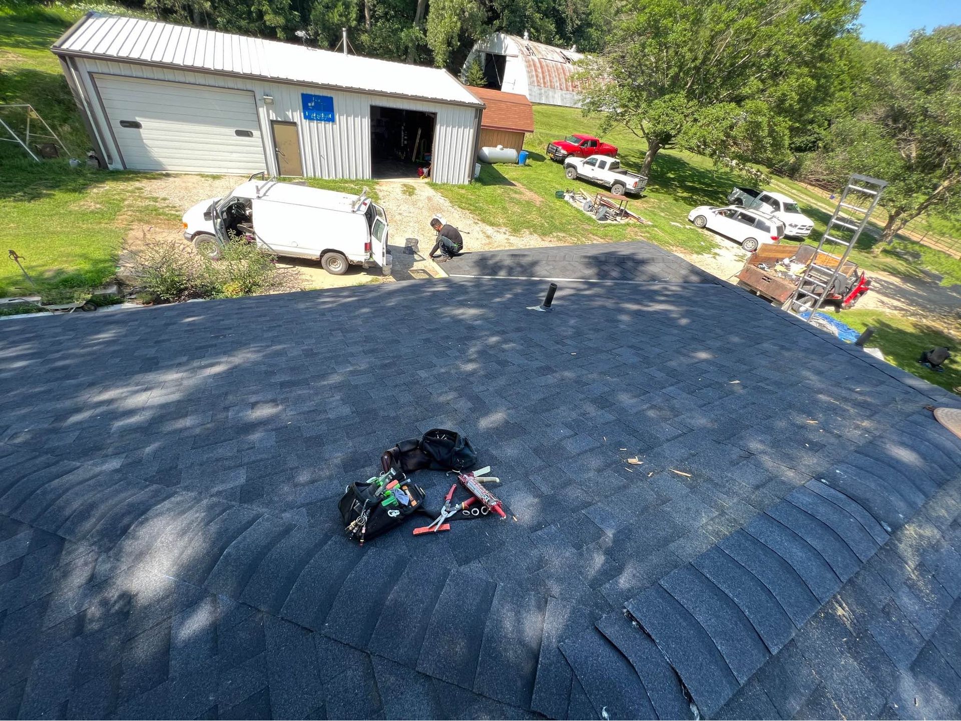 Roof being repaired with black shingles beside a garage and yard clutter.