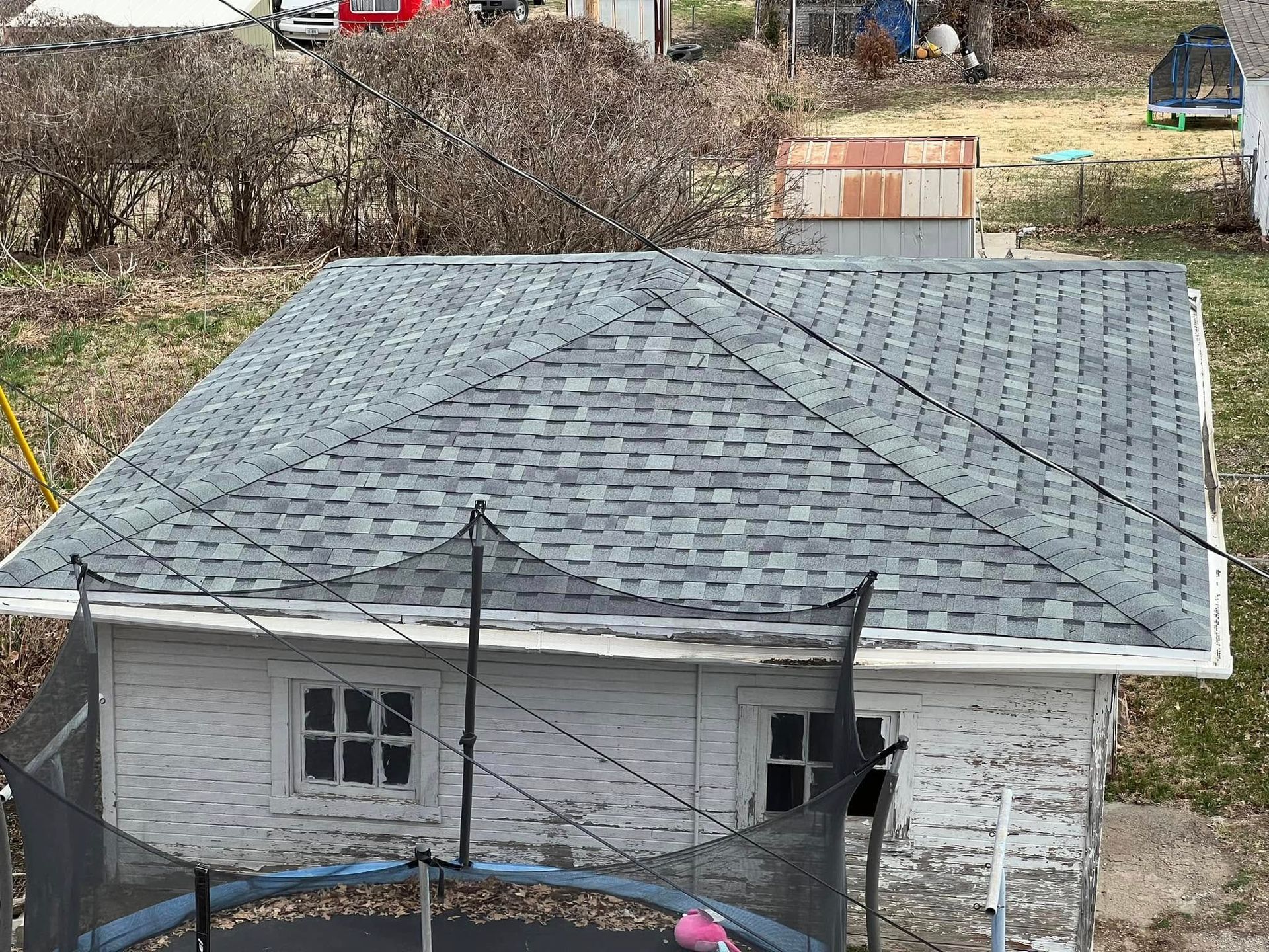 Small white house with a gray shingled roof and leafless bushes in the yard