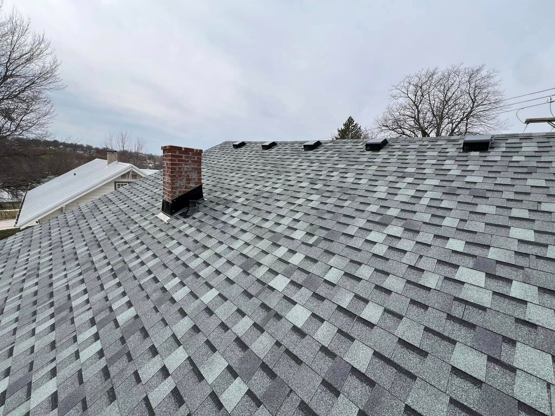 Gray shingled roof with a brick chimney under a cloudy sky