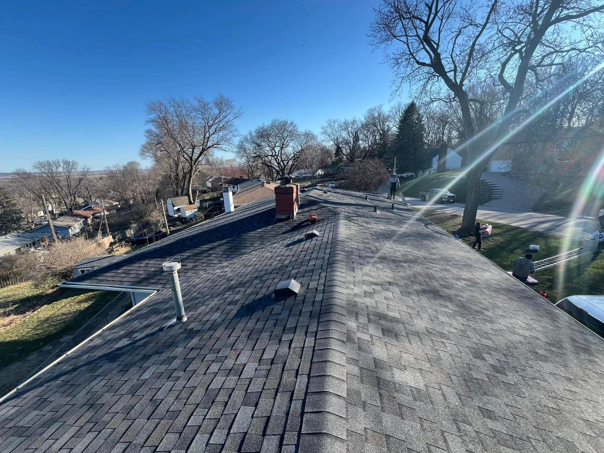 Rooftop under repair with workers, tools, and bright sunlight on gray shingles