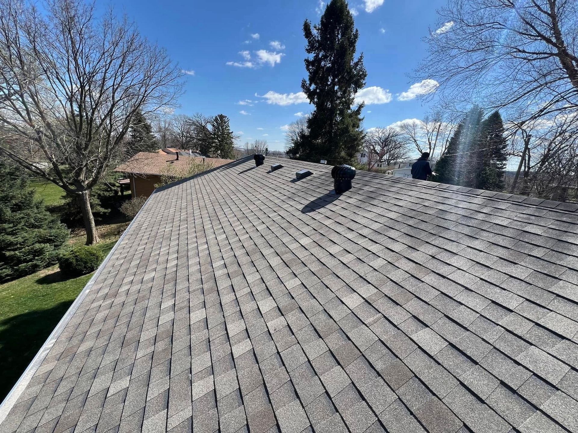 Shingled roof with three vents, viewed from above, with trees and blue sky in the background