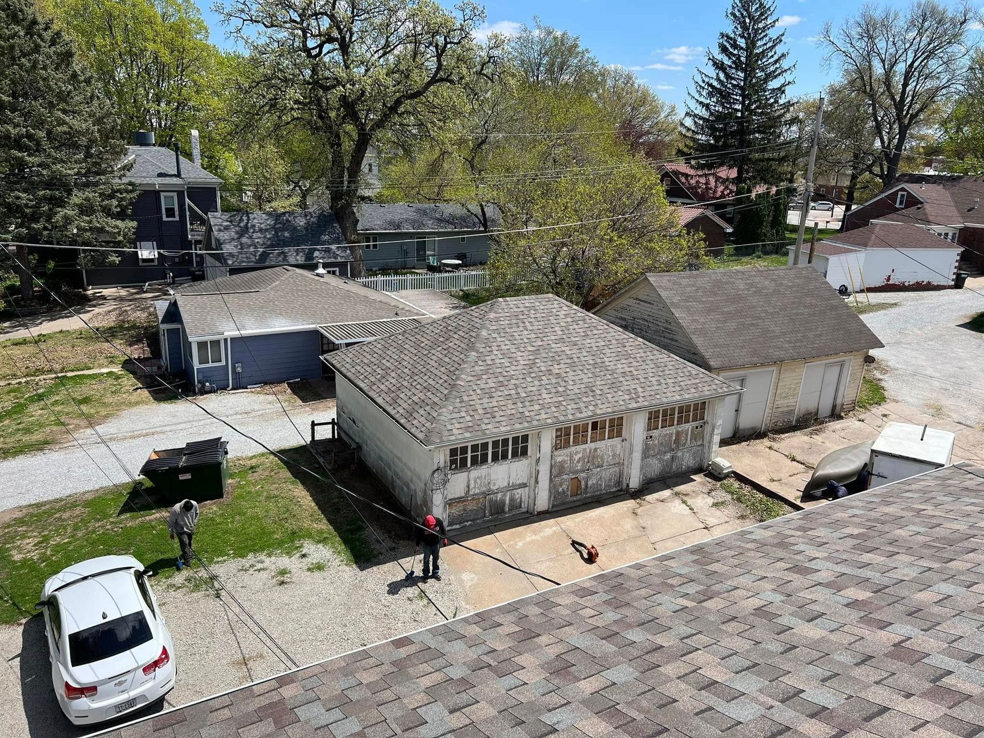 Aerial view of a small house with a driveway, parked car, and trees in a suburban neighborhood.