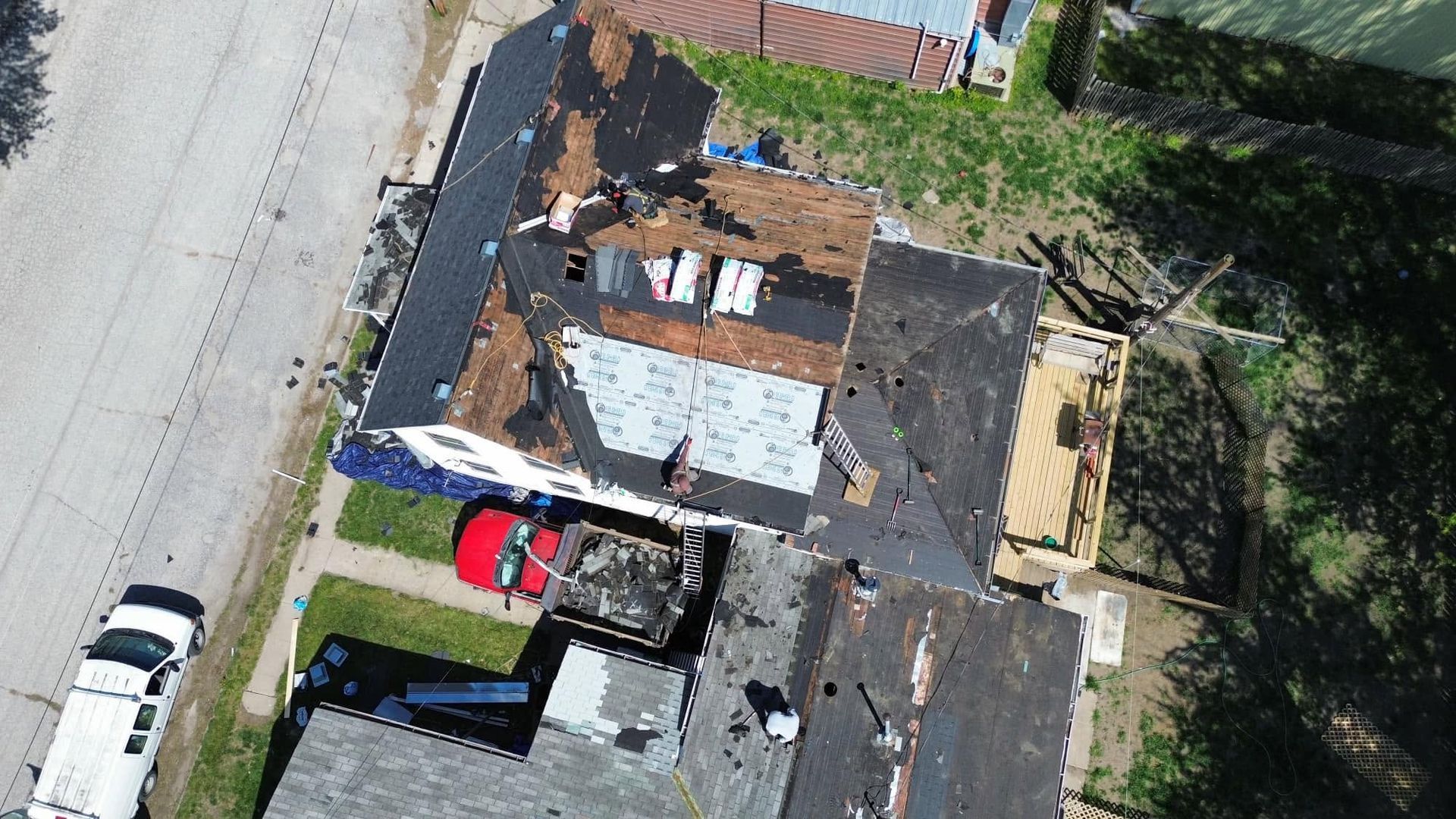 Aerial view of damaged houses beside a road, with dark roofs and parked cars nearby.