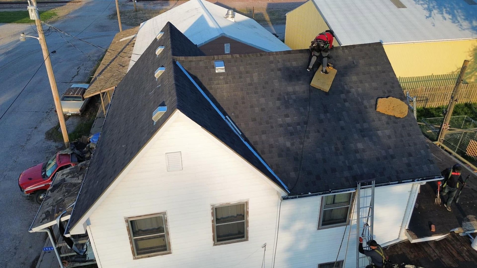 Aerial view of a white house with a dark roof, solar panels, and workers on the roof.