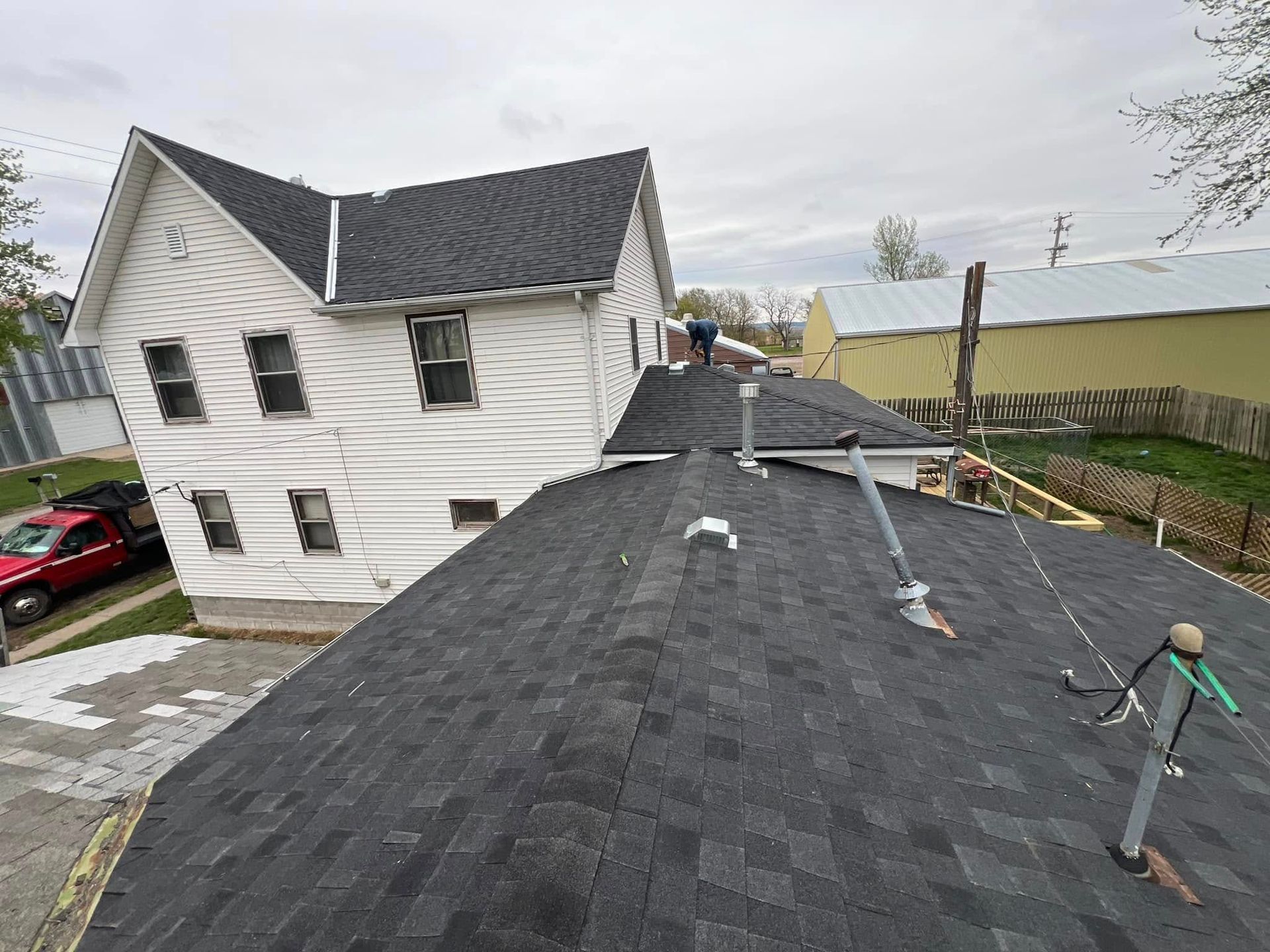 Rooftop view of a white house with dark shingles and a ladder, under overcast skies.
