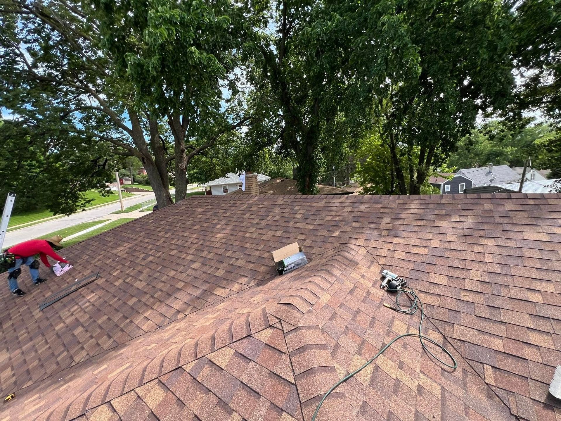 Roof shingles being repaired, with tools and a ladder on a tree-lined suburban house.