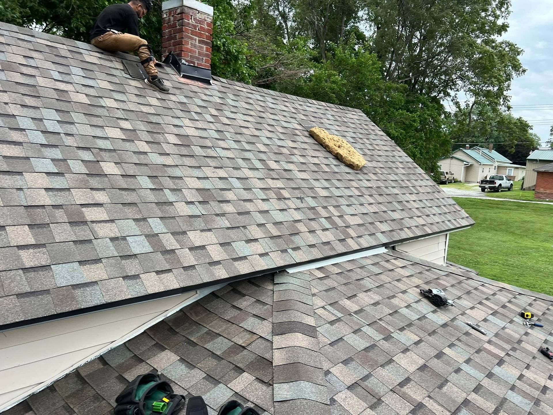 Roof being repaired with workers, missing shingles, and a green lawn below