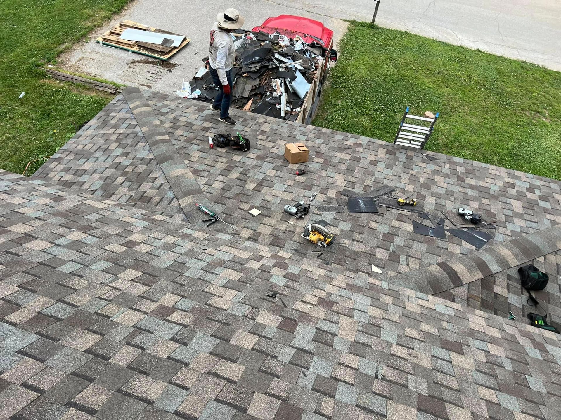 Roofers working on a shingled roof beside a red-roofed section and lawn below