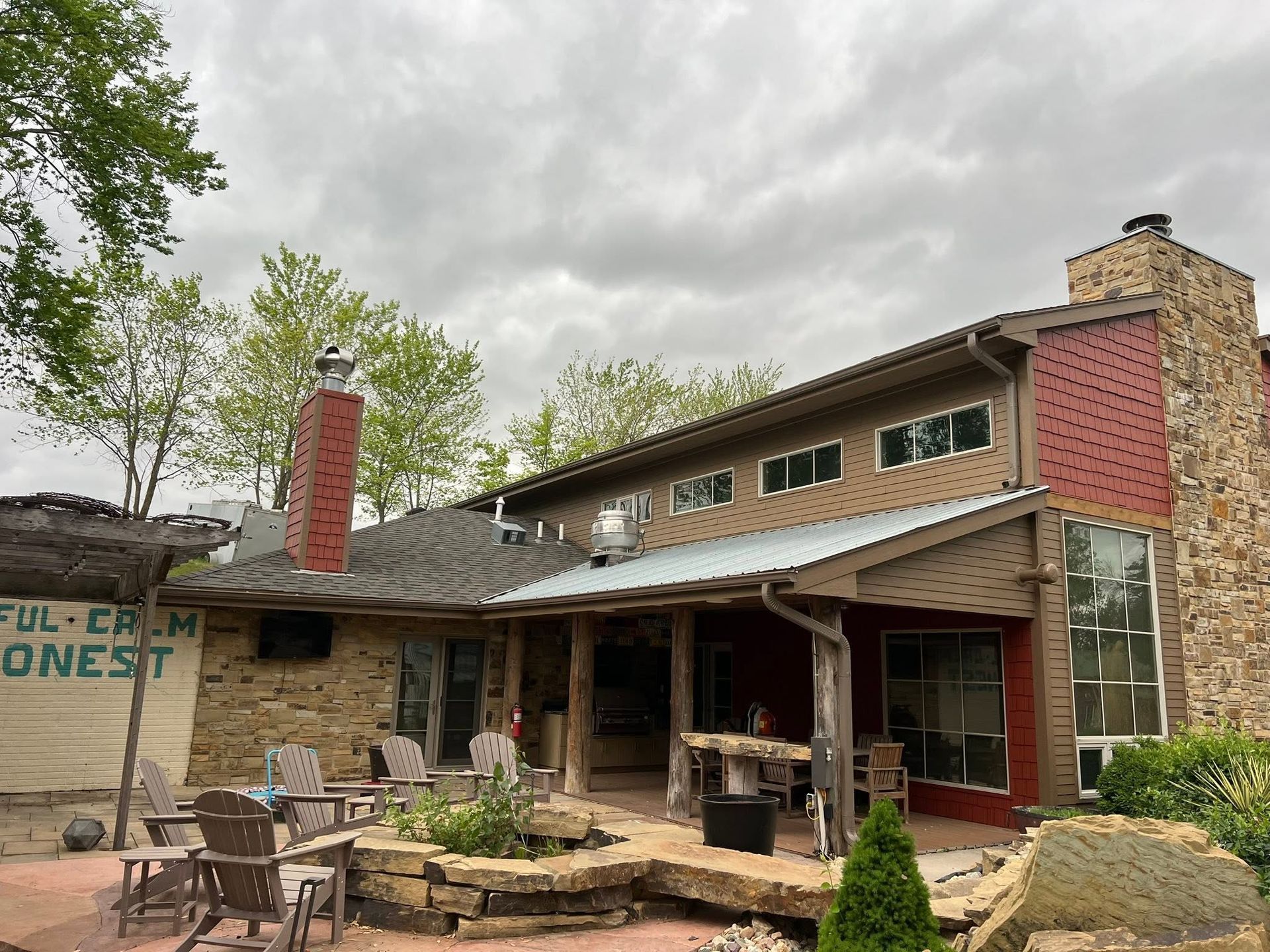 Rustic stone house with a covered porch, outdoor seating, and a chimney under an overcast sky