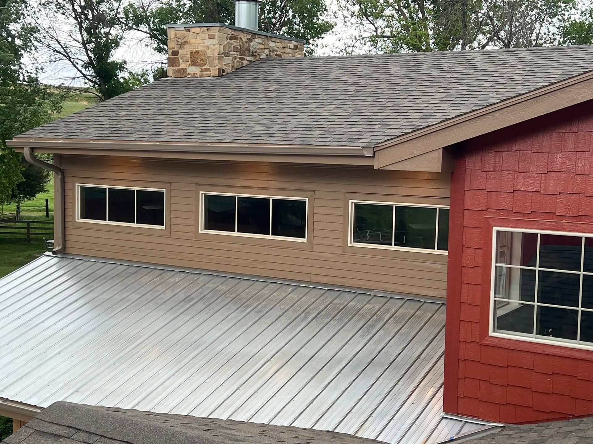 Exterior of a house with tan siding, red trim, and a light gray metal roof