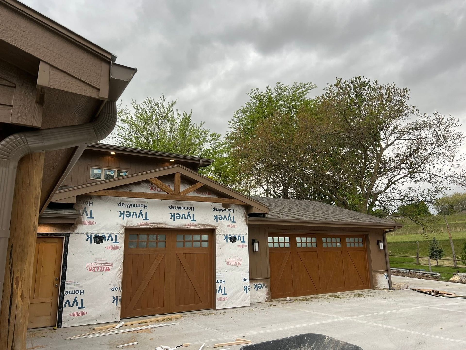 Two wooden garage doors on a small outbuilding with white siding and a stone path in front