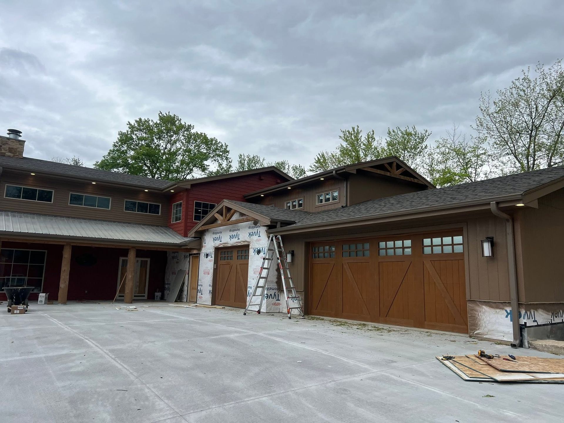 Residential house exterior with wooden garage doors and a large concrete driveway under a cloudy sky