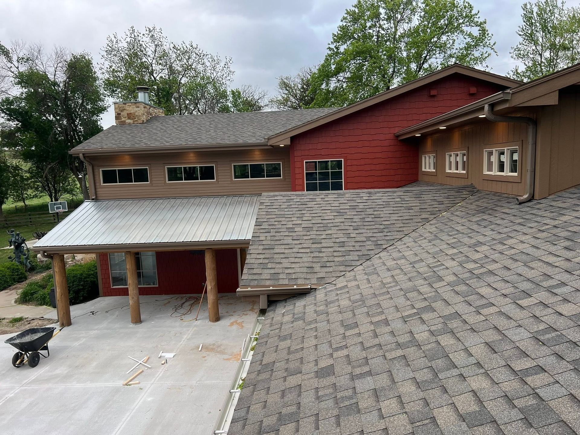 Roof repair on a red house with gray shingles and a covered driveway, viewed from above