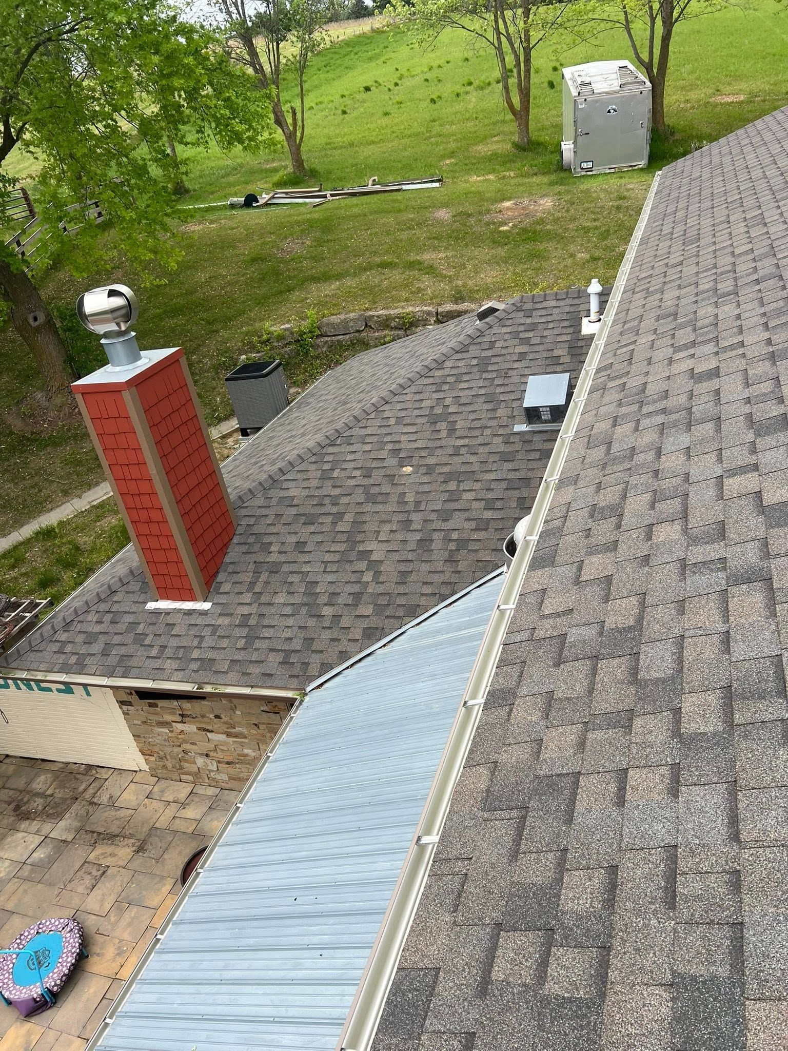 Backyard view with a red chimney, gray roof, paved patio, lawn, and utility box.