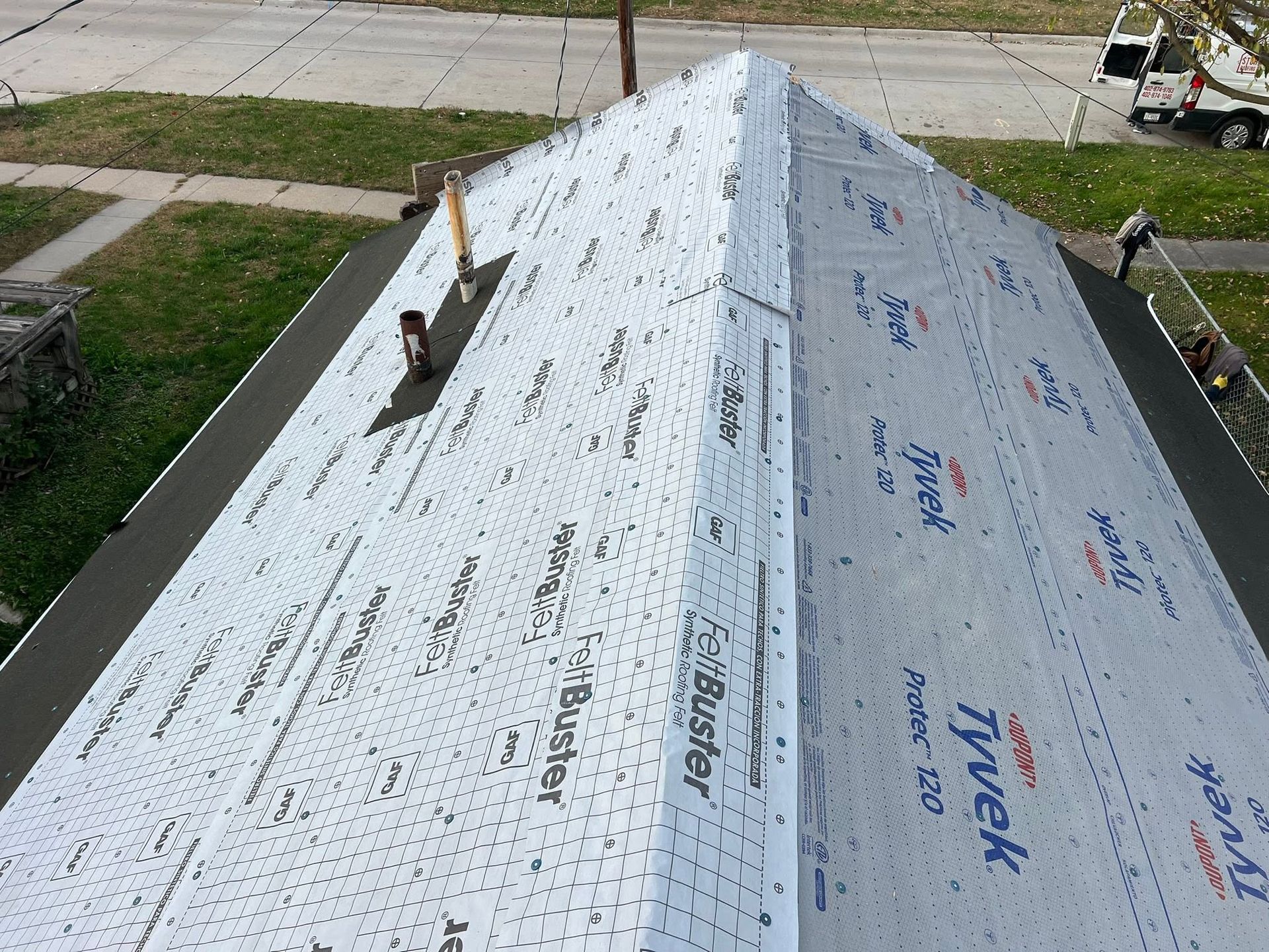 Roof under construction with white underlayment and vent pipes along the ridge, viewed from above
