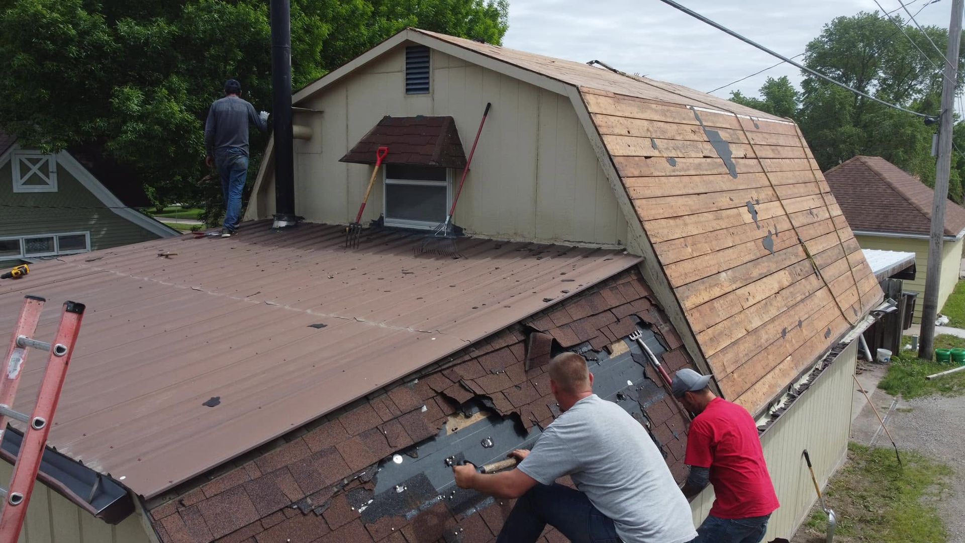 Workers repairing a damaged roof with exposed plywood and debris on a hillside house