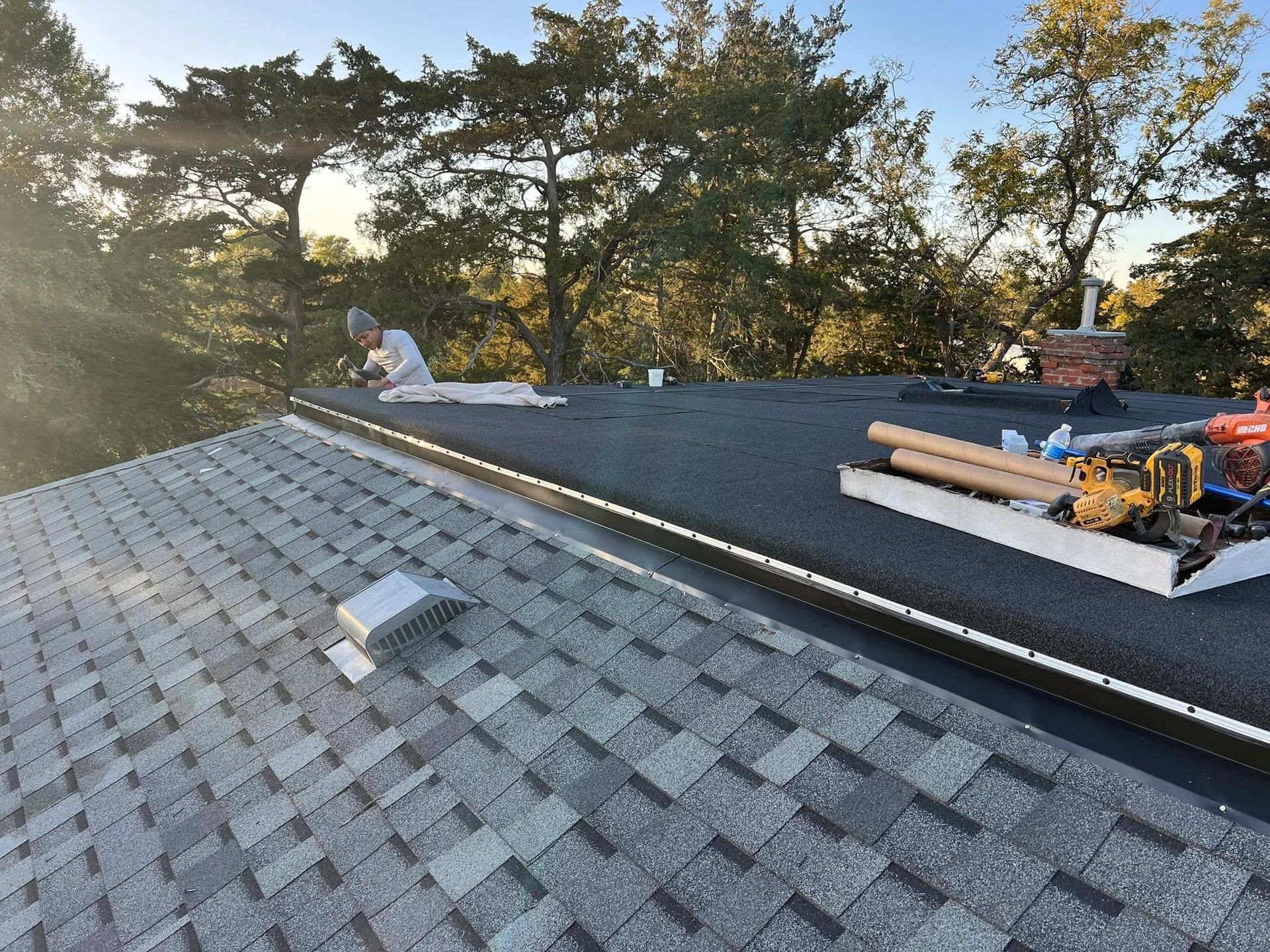 Roofing workers installing shingles on a sloped roof at sunset