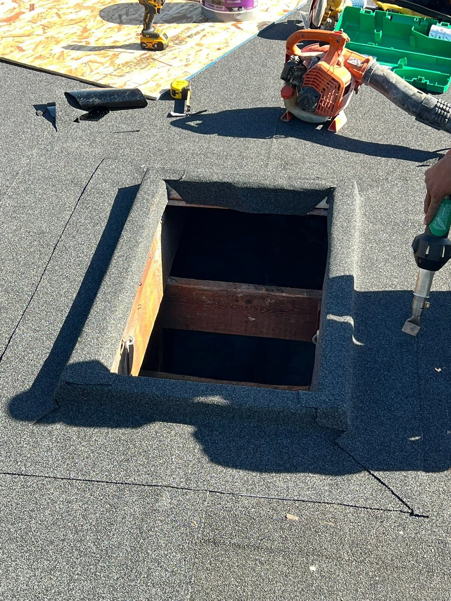 Open rooftop hatch with dark interior, surrounded by gray gravel and rooftop equipment.