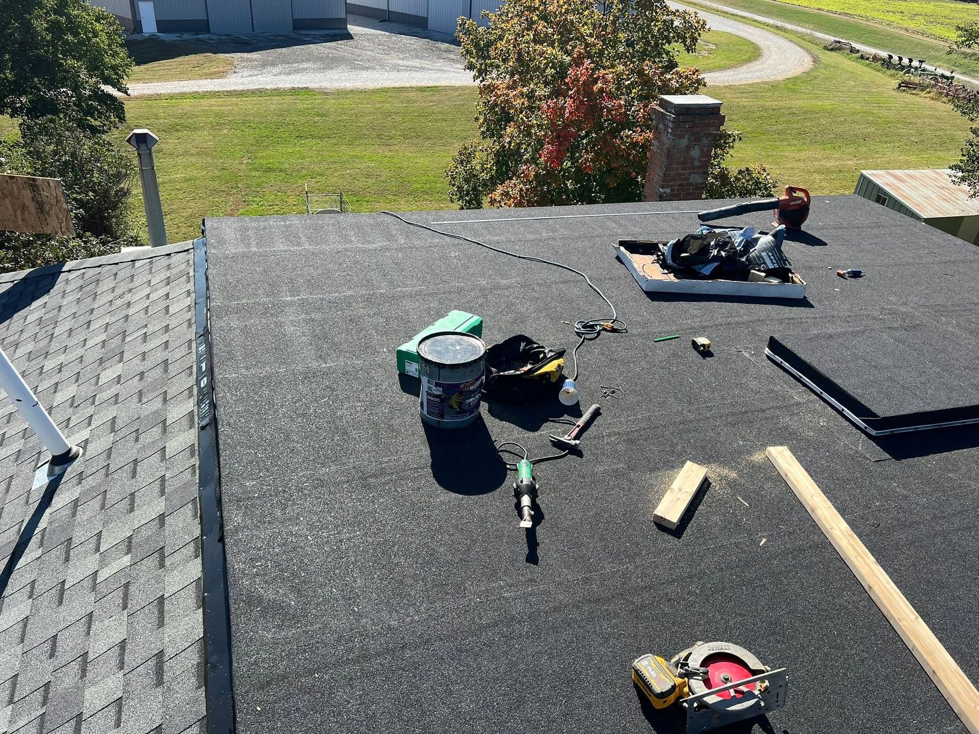 Roof with scattered tools and materials, including buckets, boards, and a toolbox, under a sunny sky.
