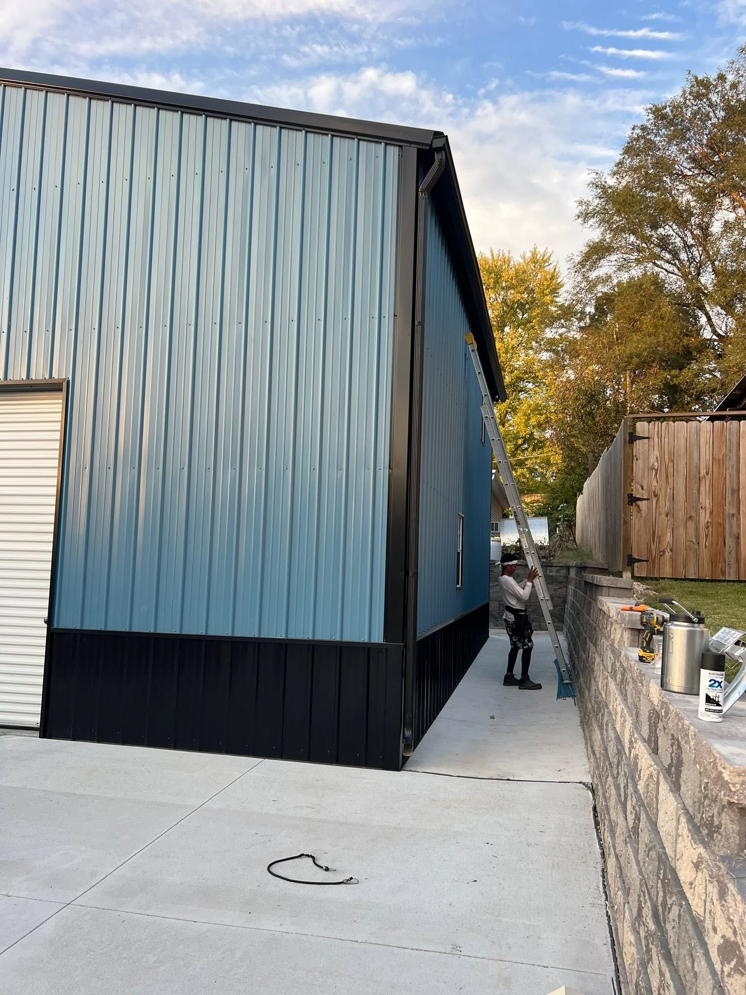 A narrow driveway beside a metal building and stone wall, with a person walking toward the back.