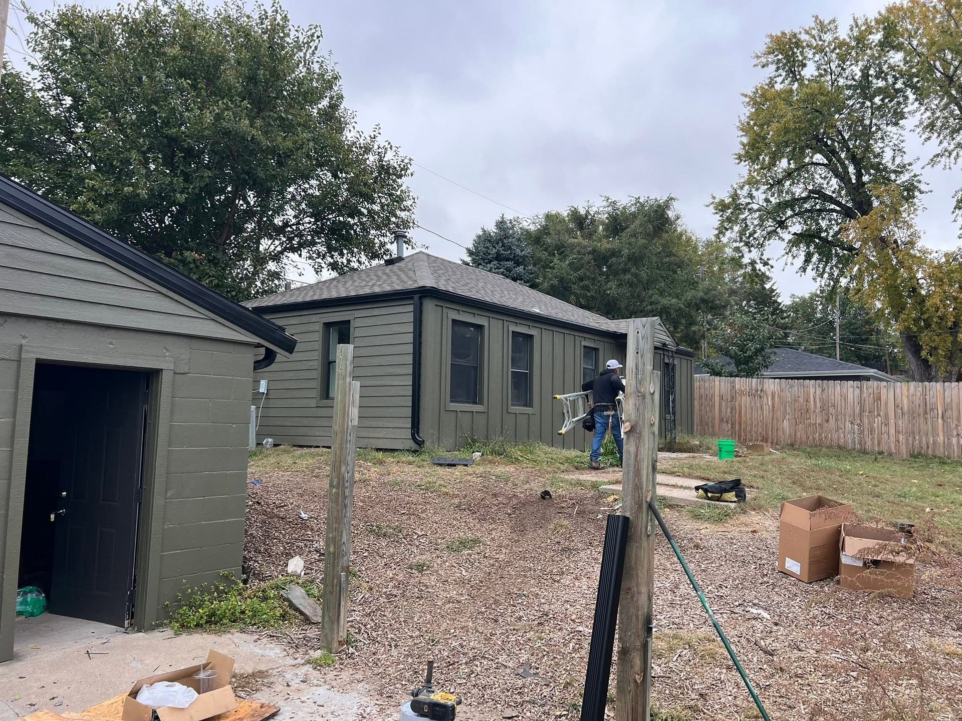 Backyard with a green shed, gravel ground, fence, trees, and a person near the house.