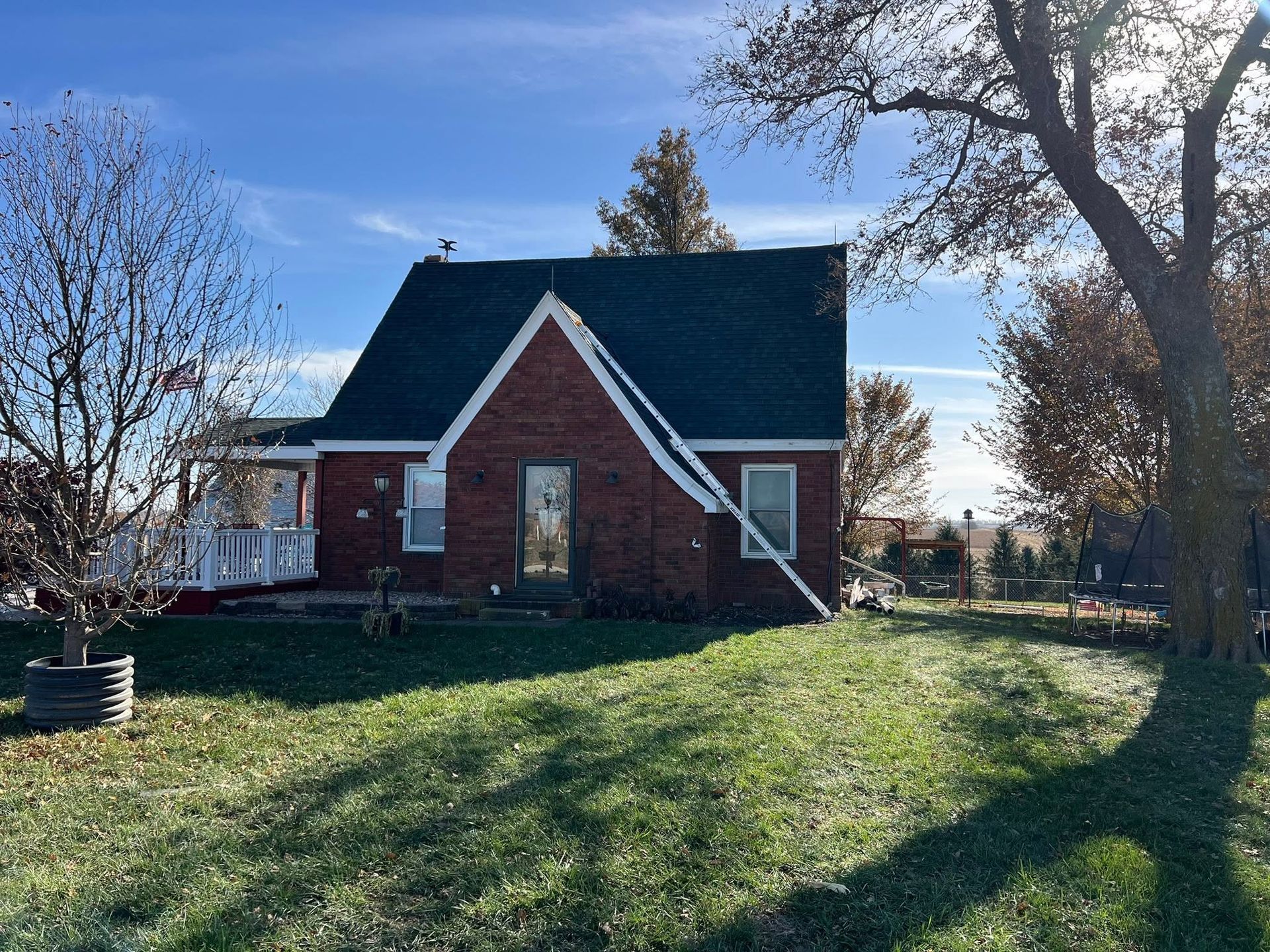 Red brick house with steep dark roof on a grassy yard under a blue sky