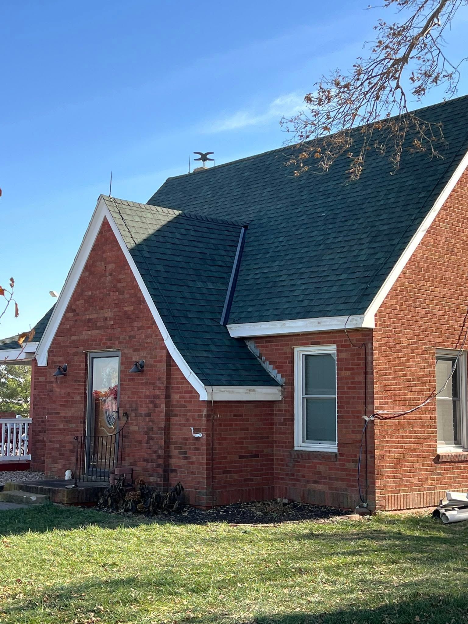 Brick house with dark green roof and white trim in a grassy yard under a blue sky