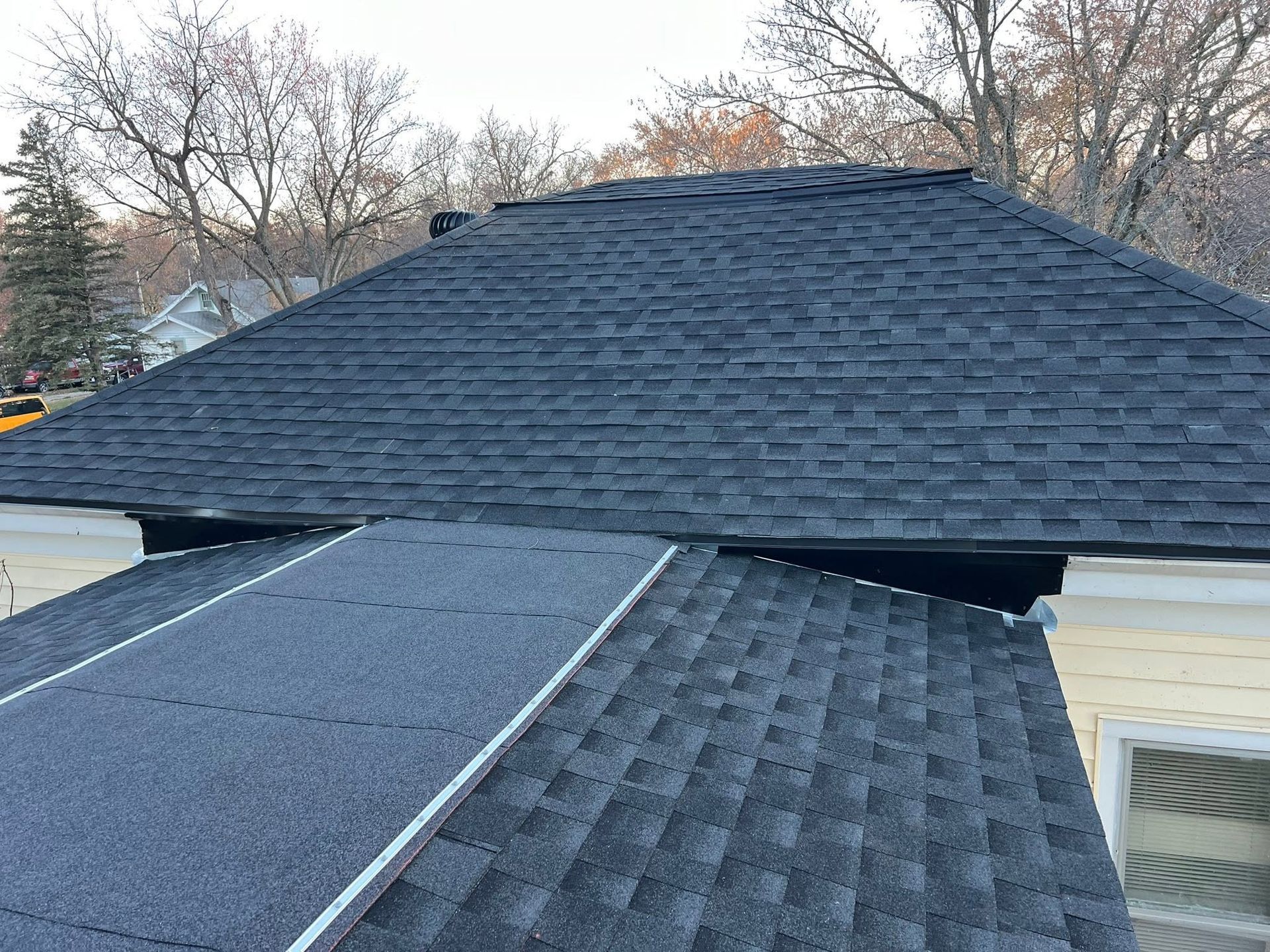 Roofing materials on a house roof, including dark shingles and a light-colored roof section under construction