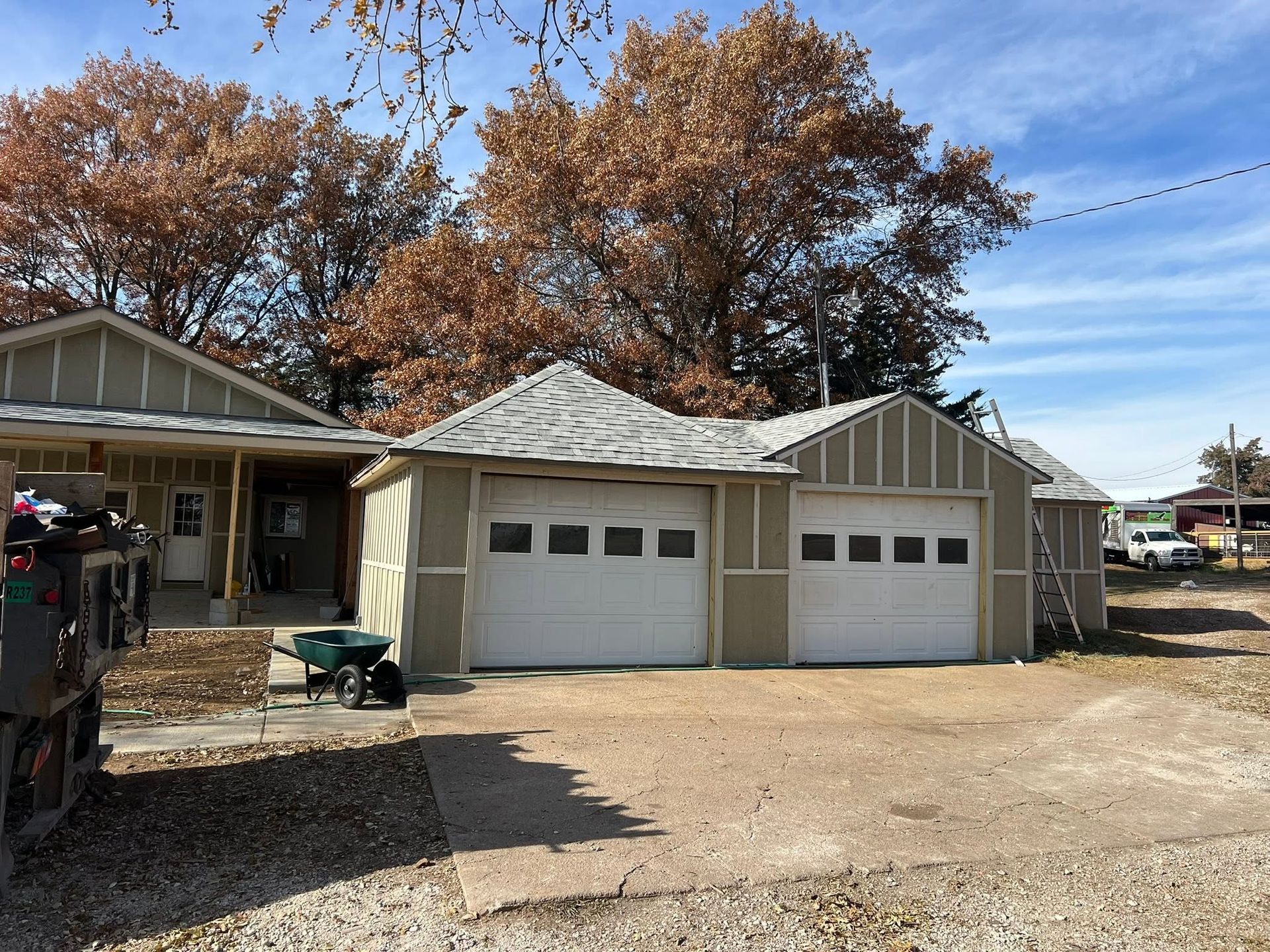 Two-car garage beside a house, with a dirt driveway and autumn trees overhead.