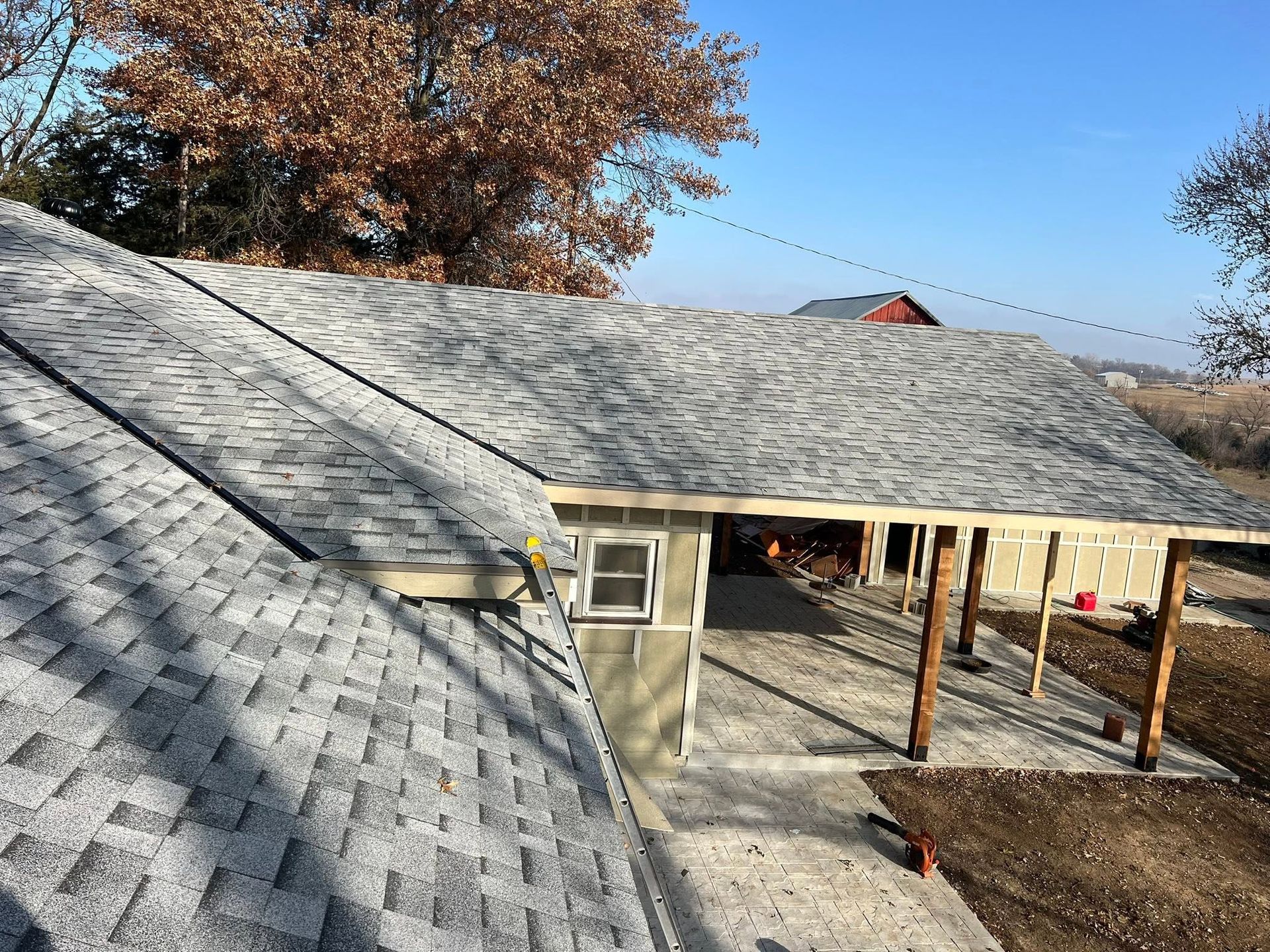 Gray shingled roof over a partially built house with exposed framing and a ladder