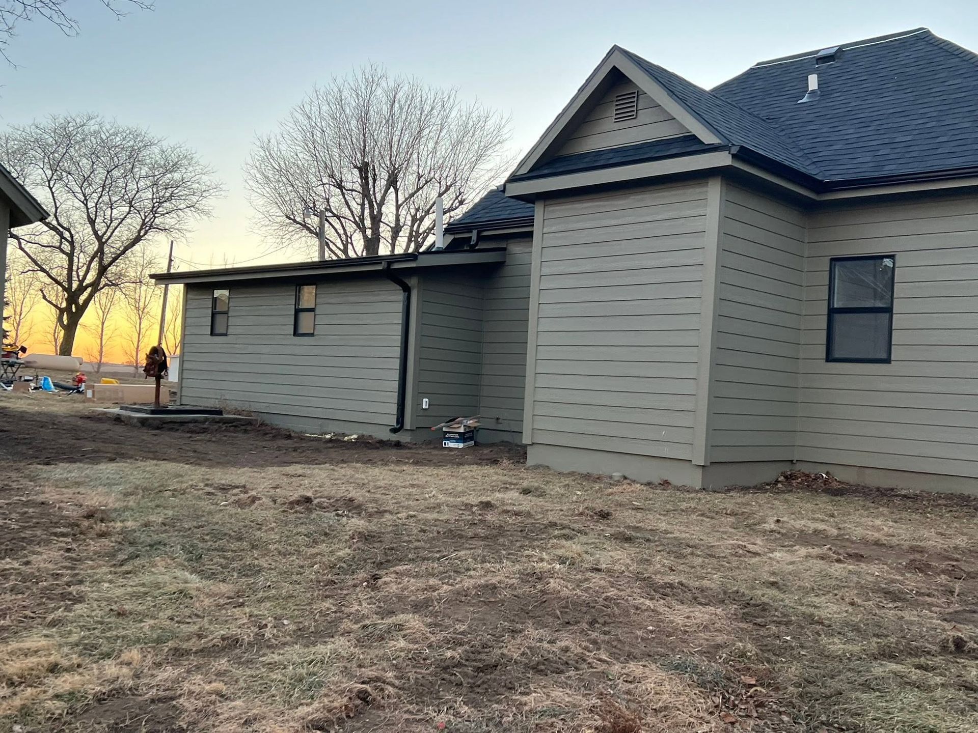 Two-story beige house with dark roof and attached garage in a bare yard at sunset