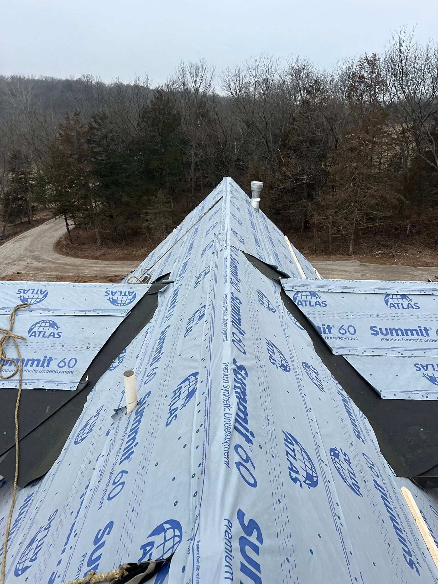 Blue tarp-covered roof ridge under construction against a wooded backdrop.
