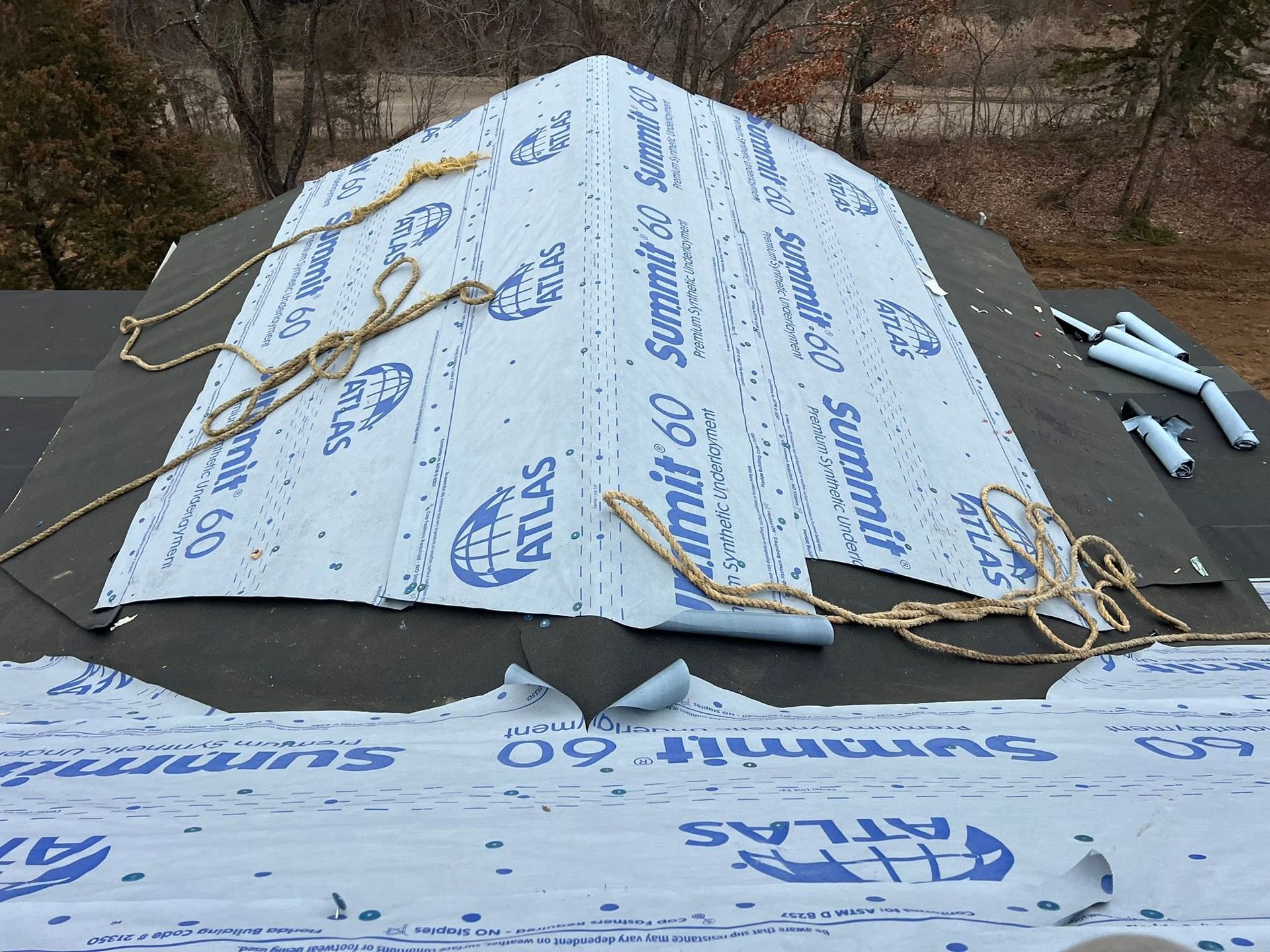 Partially covered roof with blue weatherproofing tarp and exposed shingles under repair