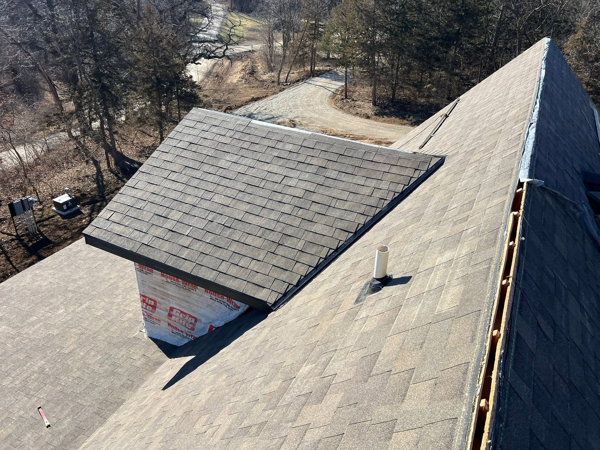 Rooftop with gray shingles and a small dormer on a sloped house, seen from above.